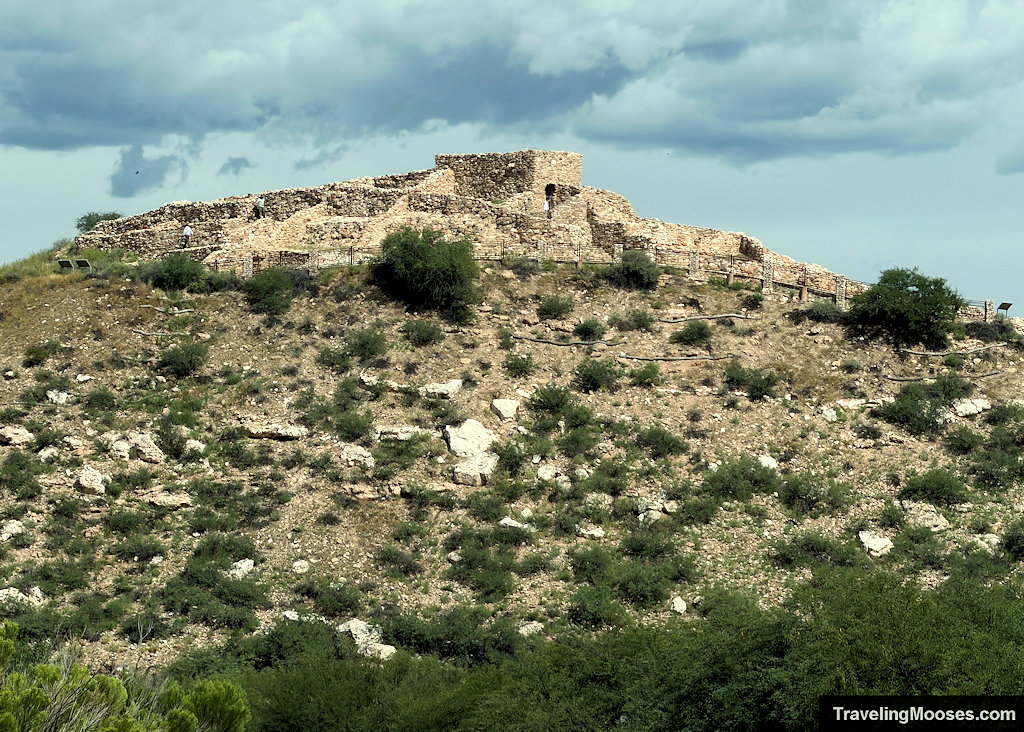 Ancient stone pueblo complex perched along the crest of a desert limestone hill under storm clouds